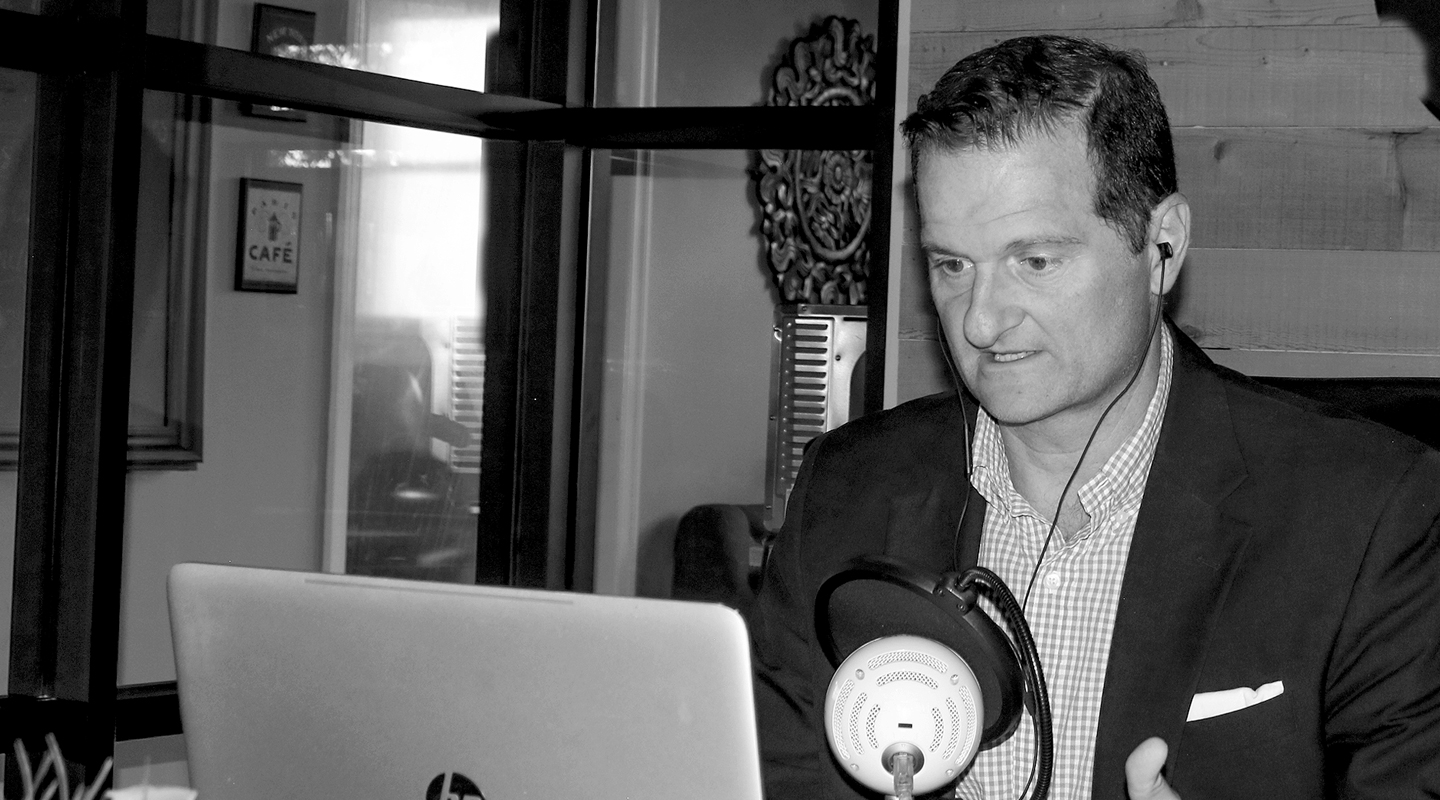 Kirk Kinder, CFP, in his office, looking at his laptop while speaking into his microphone delivering the Saving Yourself From Wall Street information and advice.